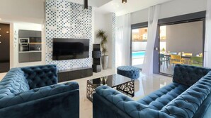 A modern living room with a large flat-screen TV, a blue sofa, and a glass coffee table. - Dots n' Stripes by Interhome (Fažana)