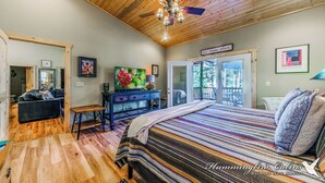 A spacious bedroom with a large bed, wooden ceiling, and a view through the door. - Spotted Owl Pet Friendly | Your Peaceful Pine Retreat w/ Owl-Worthy Views & Hot Tub Soaks (Ruidoso)