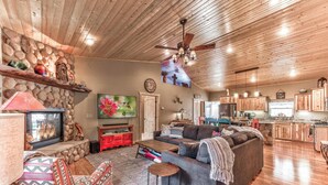 A spacious living room with a stone wall, wooden ceiling, and a large TV. - Spotted Owl Pet Friendly | Your Peaceful Pine Retreat w/ Owl-Worthy Views & Hot Tub Soaks (Ruidoso)