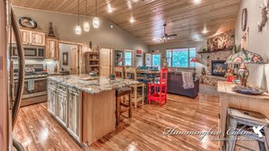 A spacious kitchen with wooden cabinets, a central island, and a dining area with a red chair. - Spotted Owl Pet Friendly | Your Peaceful Pine Retreat w/ Owl-Worthy Views & Hot Tub Soaks (Ruidoso)