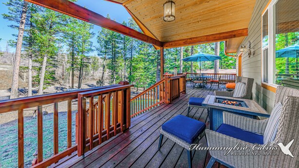 A wooden deck with wicker furniture and a fire pit, surrounded by trees. - Spotted Owl Pet Friendly | Your Peaceful Pine Retreat w/ Owl-Worthy Views & Hot Tub Soaks (Ruidoso)