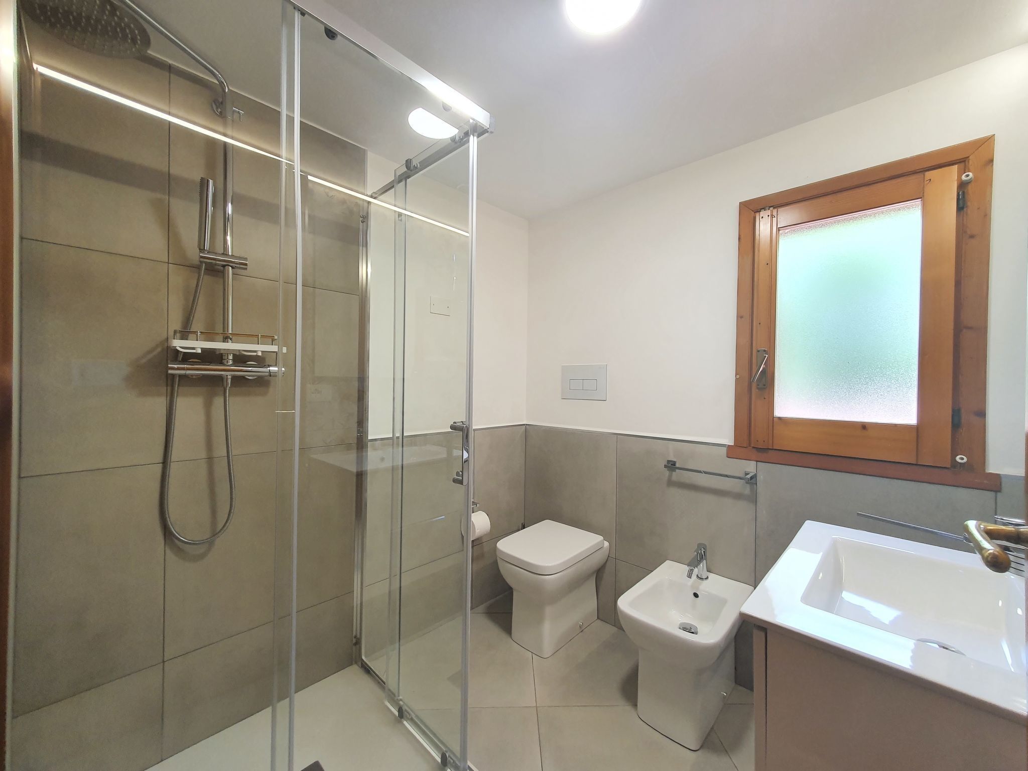 Een moderne badkamer met een douche met glazen wand, toilet, bidet en wastafel.