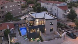 Una casa moderna de dos pisos amb piscina, terrassa coberta i un cotxe a la zona d'aparcament.