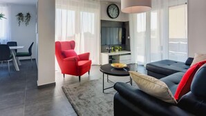 Un saló modern amb un sofà, un butac armchair vermell, una taula de centre rodona i una televisió.