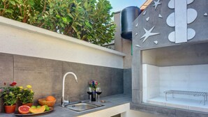 Una cuina exterior moderna amb un rentaplat, un cistell de fruita i plantes en testos.