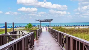 Un paseo marítimo de madera que conduce a una playa con sombrillas y una bandera.