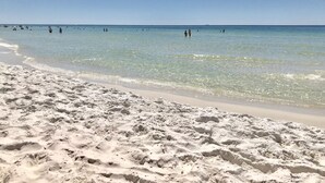 Ein Sandstrand mit klarem Wasser und badenden Menschen.