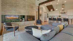 Ein modernes Wohnzimmer mit einem großen Ecksofa, einem Kamin und Blick ins Freie.