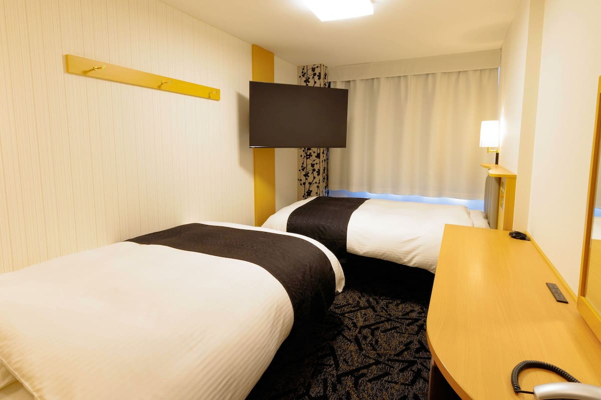 Une chambre d’hôtel avec deux lits, un bureau, une chaise, un téléviseur à écran plat et une lampe de chevet.