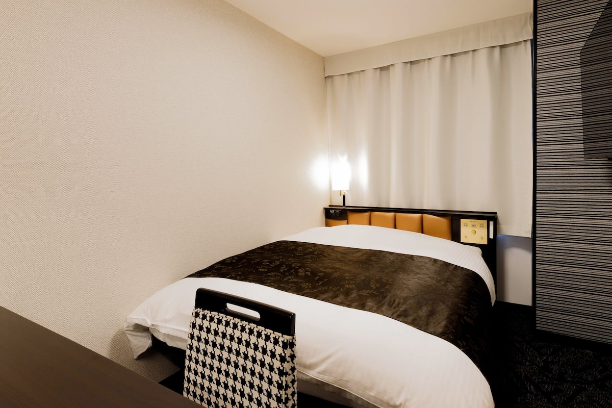 Une chambre d’hôtel avec un lit, une table de chevet, une lampe et une grande fenêtre avec des rideaux.