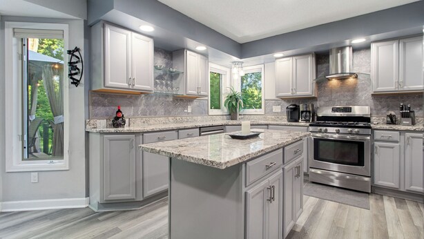 Una cocina moderna con gabinetes blancos, encimeras de granito, electrodomésticos de acero inoxidable y una isla grande.