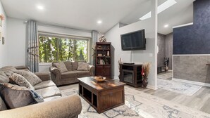 Una sala de estar con sofá, mesa de centro, televisor, estantería y chimenea.