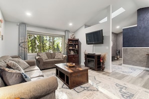 A living room with a sofa, coffee table, TV, bookshelf, and a fireplace. - Jenkins Retreat-5BR/hot tub/theater, near TPC & National Sports Center (Blaine)
