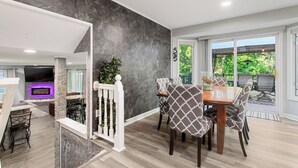Un interior moderno con zona de comedor, una pared de acento de piedra y vistas a través de puertas de cristal.