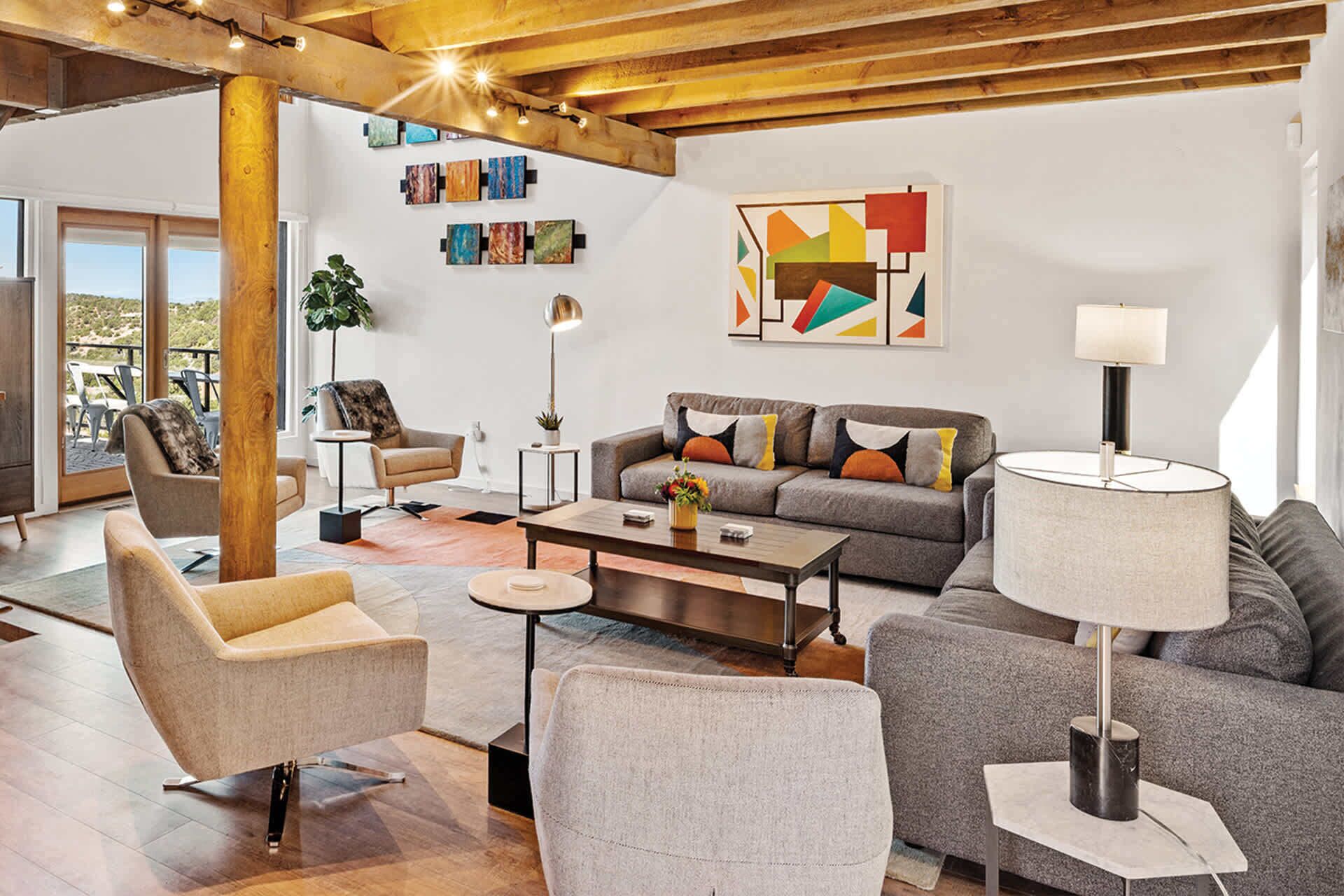 Un salon moderne comprenant un canapé, des fauteuils, une table basse et un lampadaire. Les murs sont ornés de tableaux abstraits et une grande fenêtre laisse entrer la lumière naturelle.