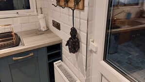 Una cocina con paredes de azulejos blancos, un perchero de madera con ganchos, un radiador y una ventana con vistas al exterior.