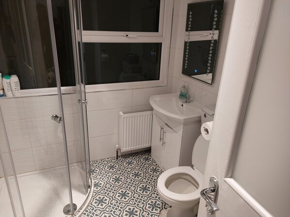 Een badkamer met douche, toilet, wastafel en vloertegels met een patroon.