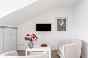 Een moderne kamer met een witte tafel, een bloemenvaas, een flatscreen televisie en een schilderij aan de muur.