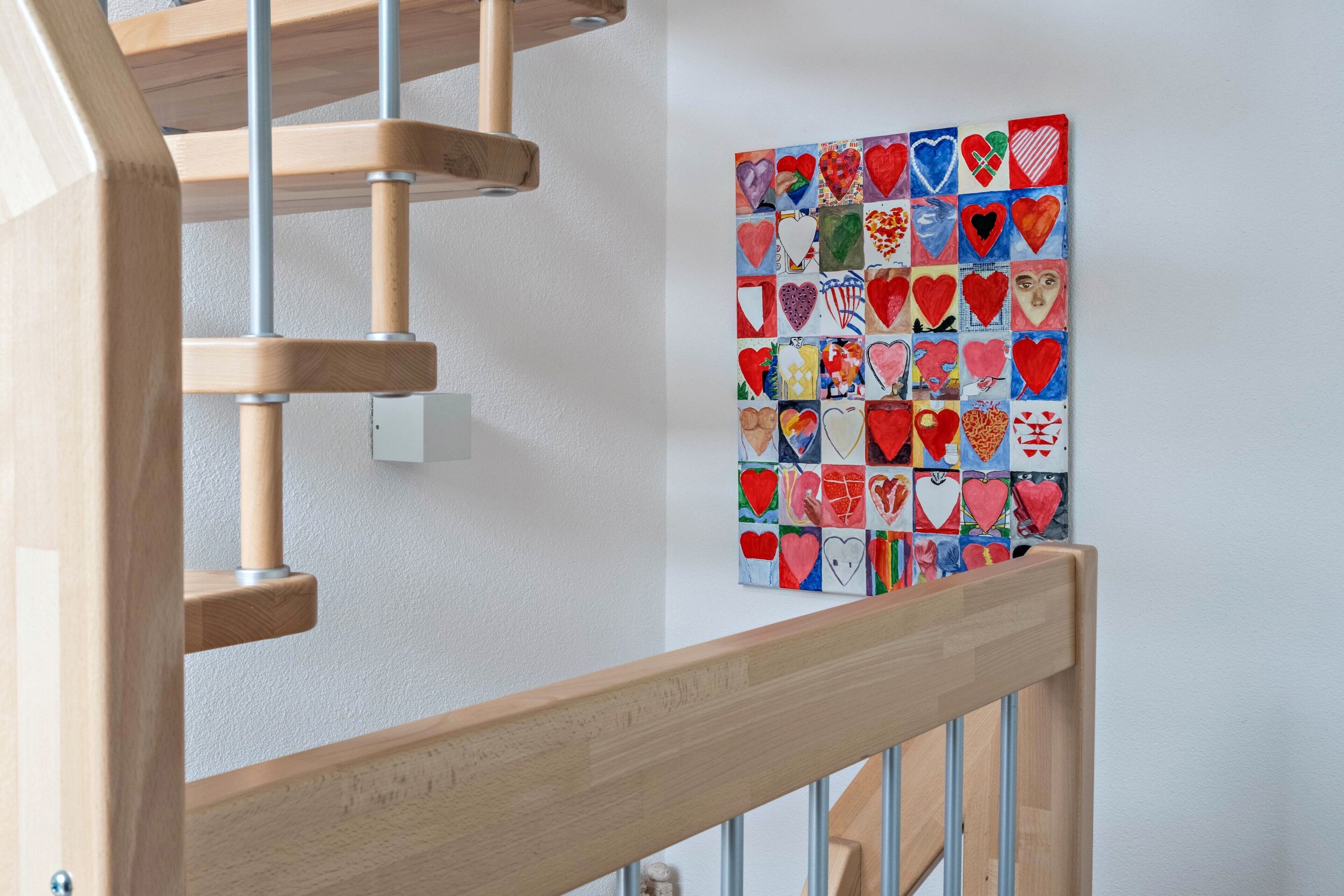 A wooden staircase with a handrail, a wall-mounted heart-patterned artwork, and a light switch.