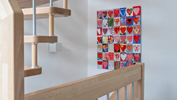 A wooden staircase with a handrail, a wall-mounted heart-patterned artwork, and a light switch.