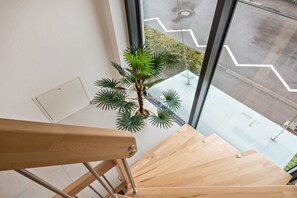 A wooden staircase with a potted plant, a window with a view of a parking lot, and a metal handrail.