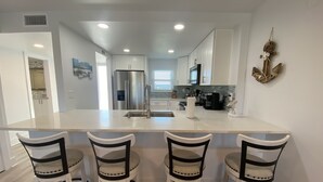 A modern kitchen with a central island, three bar stools, stainless steel appliances, and a decorative wreath on the wall. - 🦩Book Me Baby! Gulf View ~ It's The Treasure You Have Been looking For!🦩 (Fort Walton Beach)