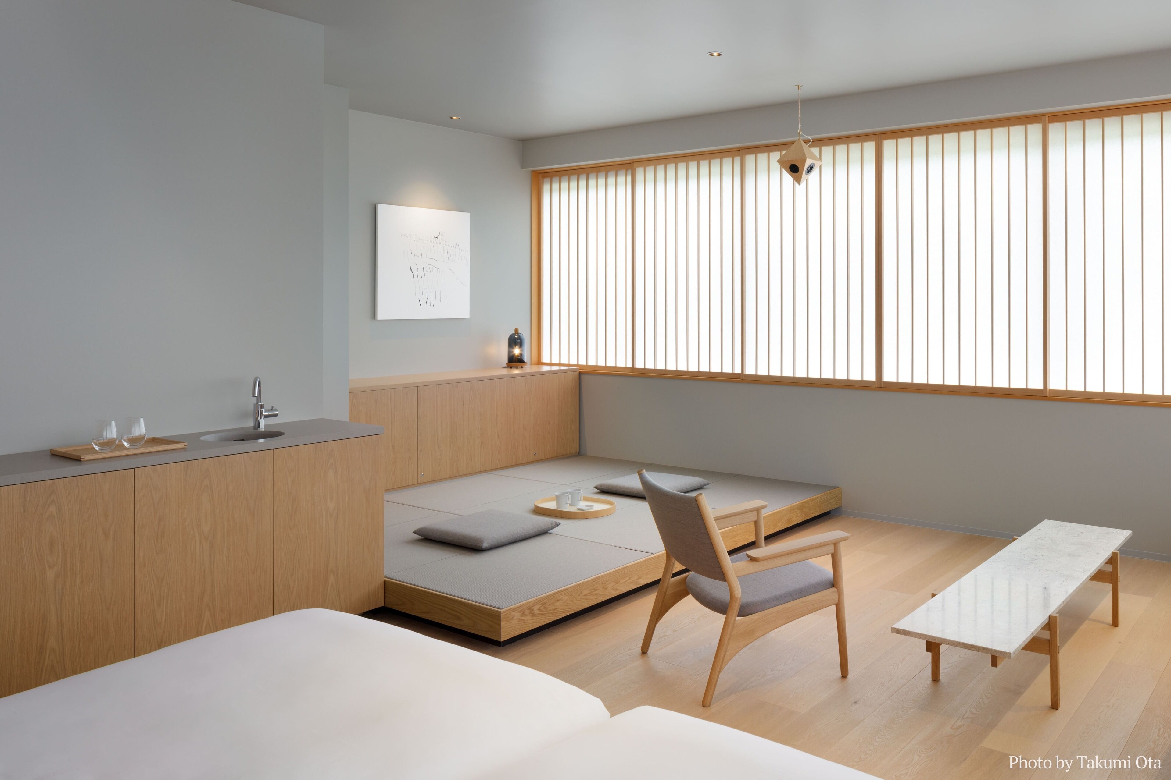 Une chambre à coucher moderne et minimaliste, comprenant un lit, un canapé-lit, un banc en bois et une petite table.