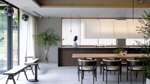 Een moderne keuken met een houten kookeiland, hanglampen en uitzicht op iemand die aan de balie werkt.