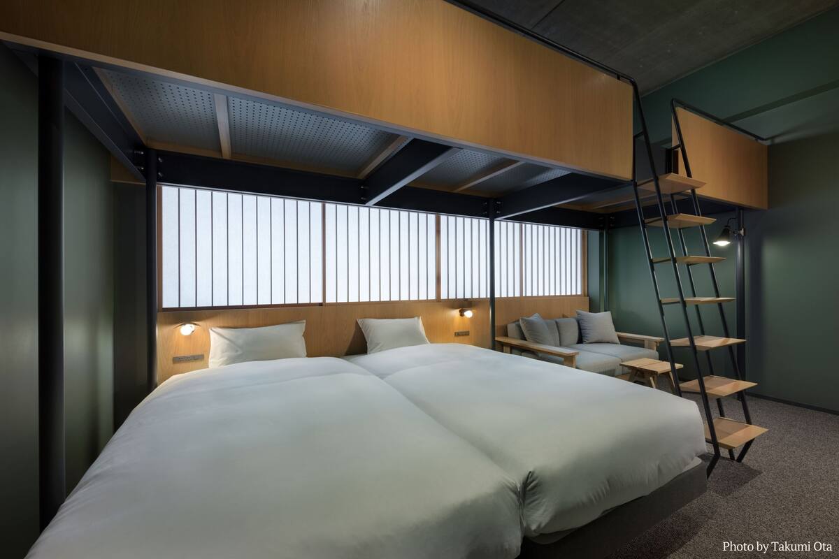 Een moderne hotelkamer met een groot bed, een bureau, een stoel, een ladder en een raam met jaloezieën.