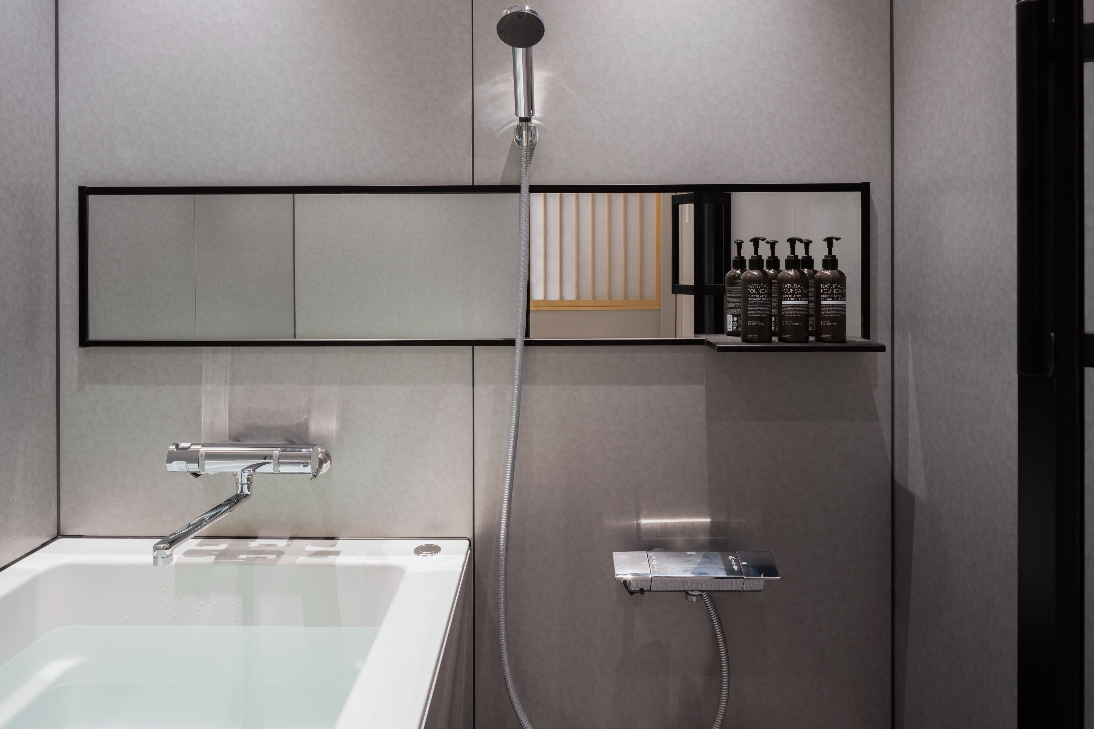 Un baño moderno con bañera de hidromasaje con mampara de vidrio, cabezal de ducha manual y estante con artículos de aseo.