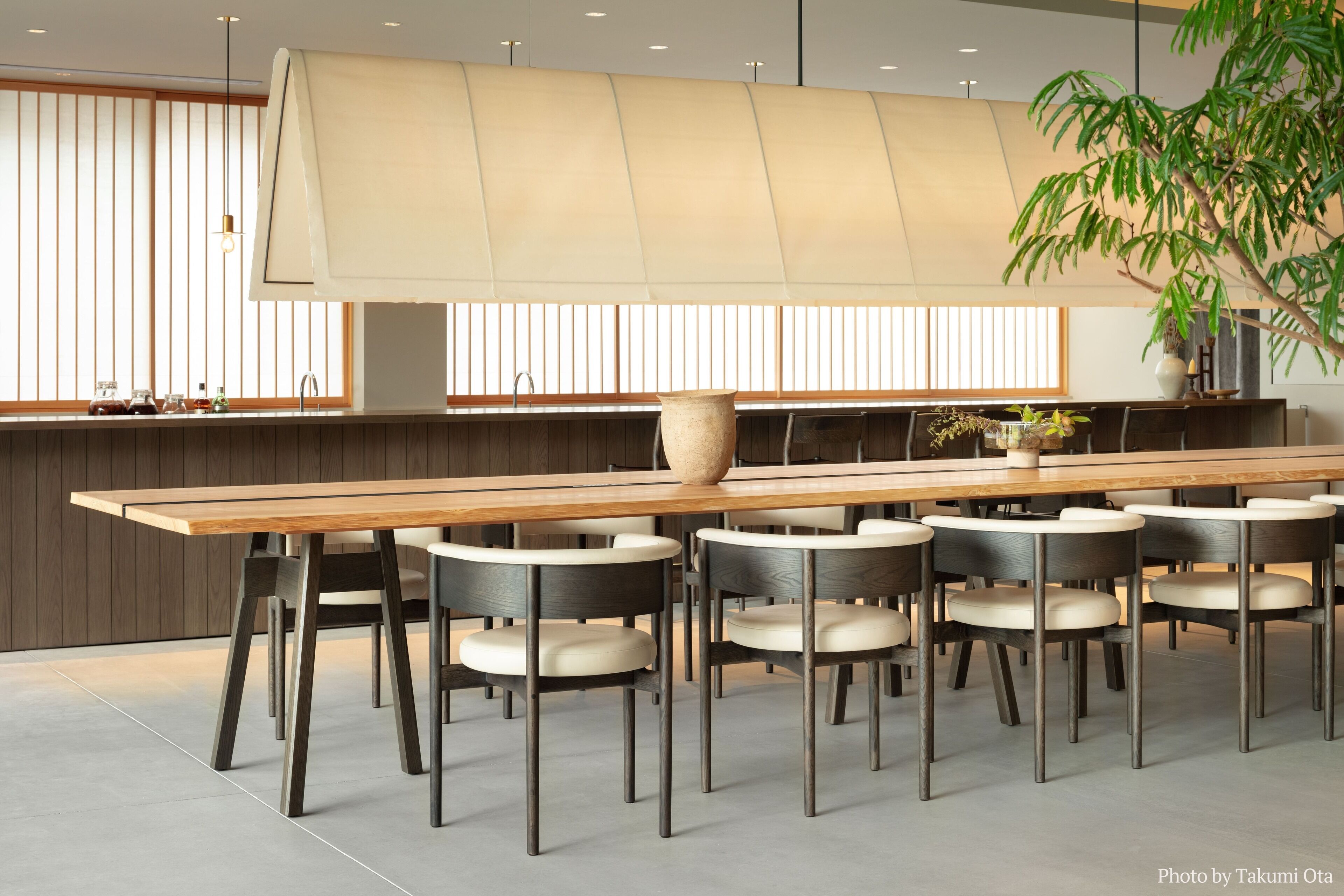 A modern dining area with a long wooden table, multiple chairs, and a large vase.