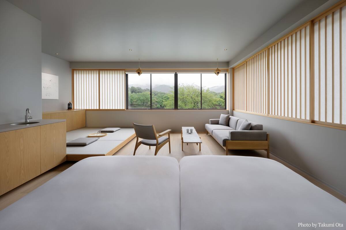 Een moderne kamer met een bank, een stoel, een klein tafeltje en uitzicht op groen door grote ramen.