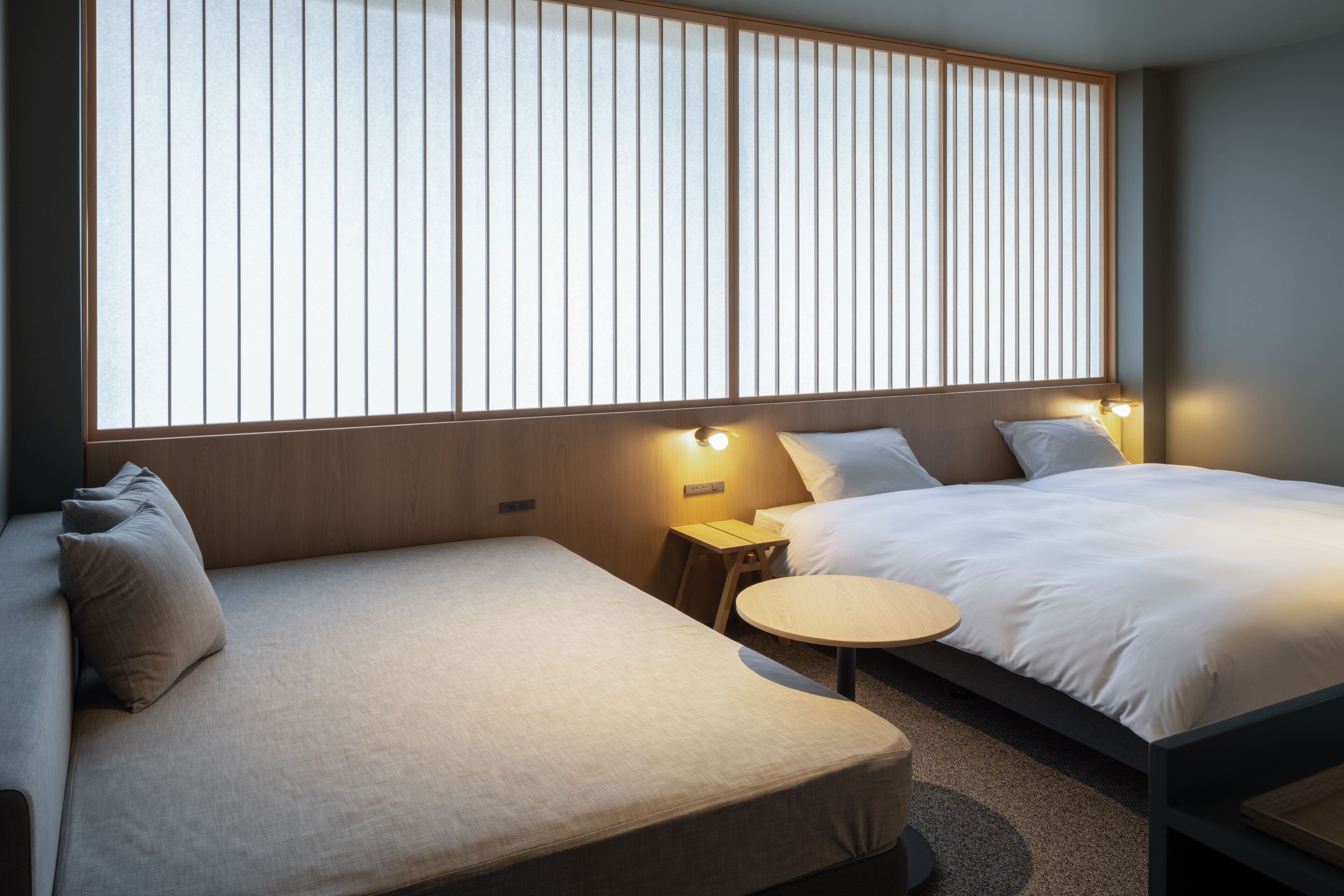 A hotel room with a large window, a sofa, a bed, and a small round table.
