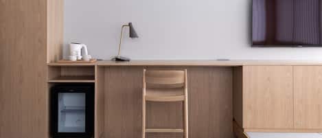 A minimalist room with a wooden desk, a chair, a television, and a small refrigerator.