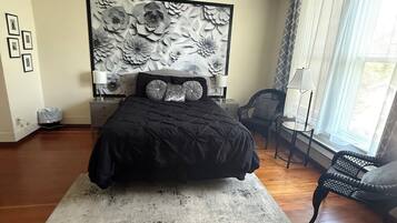 A bedroom with a large bed, a nightstand, a chair, a window with curtains, and a wall with a floral pattern.