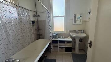 Et badeværelse med badekar, et vindue, en vask og et bruseområde.