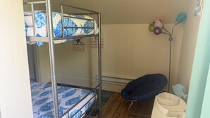 Uma cama beliche com roupa de cama estampada, uma cadeira, um abajur e uma prateleira na parede com objetos decorativos.