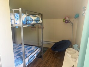 Un lit superposé avec une literie à motifs, une chaise, une lampe sur pied et une étagère murale agrémentée d’objets décoratifs.