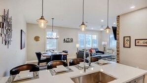 Una cocina moderna con una isla central, iluminación colgante y una zona de comedor con mesa y sillas.