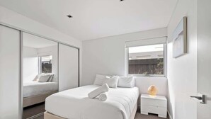 Un dormitorio moderno con una cama grande, una mesita de noche, un espejo y una ventana.