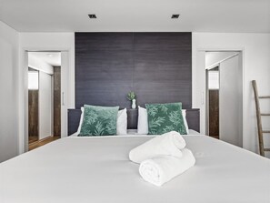 A modern hotel room with a large bed, dark headboard, and two green pillows.