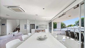 Un interior moderno con una larga mesa de comedor, muebles blancos y una zona de cocina.