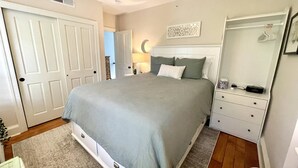 Ein Schlafzimmer mit Bett, Nachttisch, Kommode, Spiegel und einer Tür.