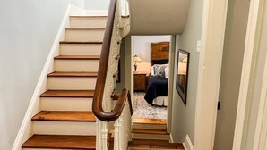 Eine Treppe mit Holzboden und einer weißen Handläufe, die zu einem Schlafzimmer mit einem Bett, einem Nachttisch und einer Lampe führt.