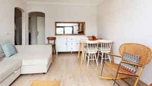 A modern living room with a sofa, dining table, chairs, and a wicker rocking chair. - Adelfa 7 by Interhome (L'Escala)