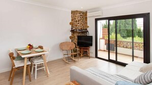 A modern living room with a sofa, a dining table with chairs, a TV, and a stone wall. - Adelfa 7 by Interhome (L'Escala)