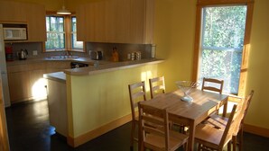 A kitchen with wooden cabinets, a built-in microwave, a sink, and a dining area with a wooden table and chairs. - Modern Craftsman Style House in Hyde Park, Austin (Austin)