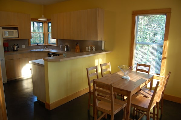 A kitchen with wooden cabinets, a built-in microwave, a sink, and a dining area with a wooden table and chairs.