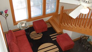 A room with a large window, a red sofa, a small table, and a lamp. - Modern Craftsman Style House in Hyde Park, Austin (Austin)