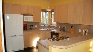 A modern kitchen with wooden cabinets, a white refrigerator, a microwave, a sink, a dishwasher, a stove, and a window providing natural light. - Modern Craftsman Style House in Hyde Park, Austin (Austin)